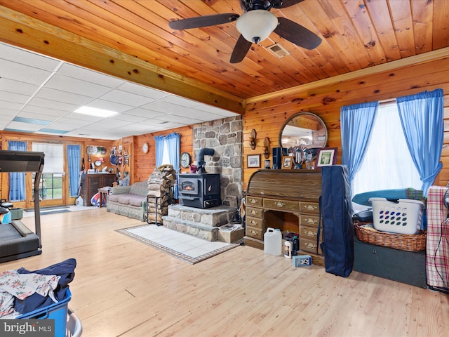 living room with light wood-type flooring, wooden walls, a wood stove, and a healthy amount of sunlight