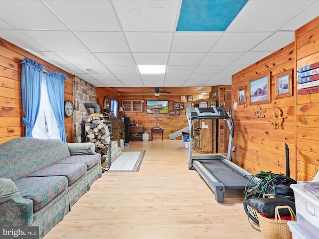 workout area with a paneled ceiling, ceiling fan, wood walls, and light wood-type flooring