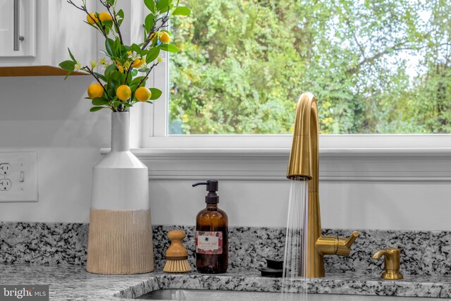 interior details featuring light stone counters, sink, and white cabinets