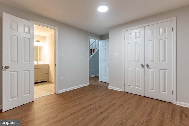 unfurnished bedroom with connected bathroom, a closet, and hardwood / wood-style flooring