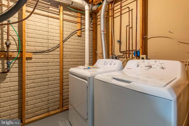 laundry room featuring brick wall and washing machine and clothes dryer