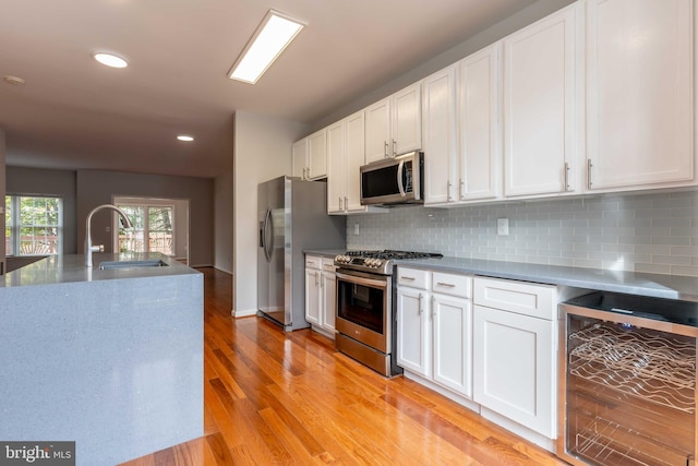 kitchen with stainless steel appliances, beverage cooler, sink, light hardwood / wood-style floors, and white cabinetry