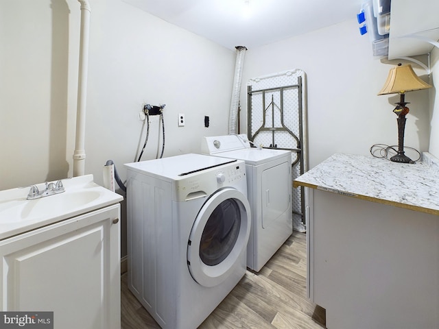 laundry area featuring cabinets, washing machine and clothes dryer, sink, and light hardwood / wood-style flooring