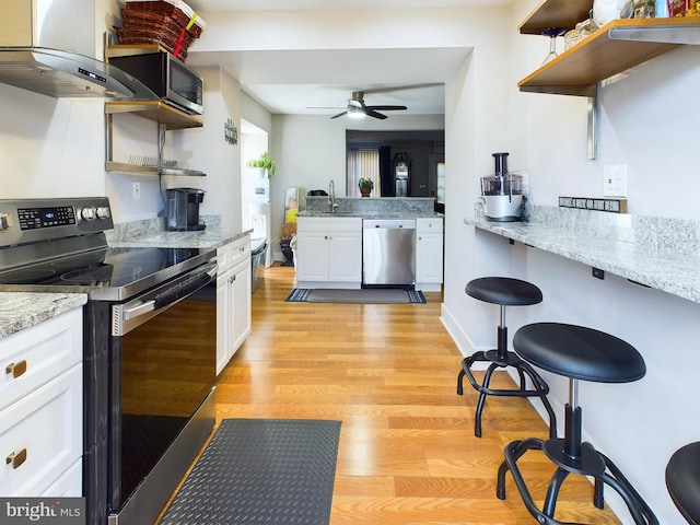 kitchen with stainless steel appliances, light stone counters, extractor fan, light hardwood / wood-style floors, and white cabinets