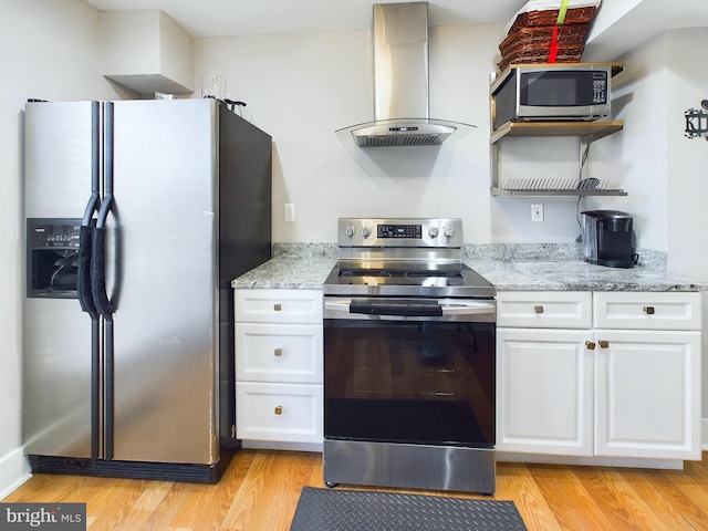 kitchen with white cabinets, light hardwood / wood-style flooring, wall chimney exhaust hood, and appliances with stainless steel finishes