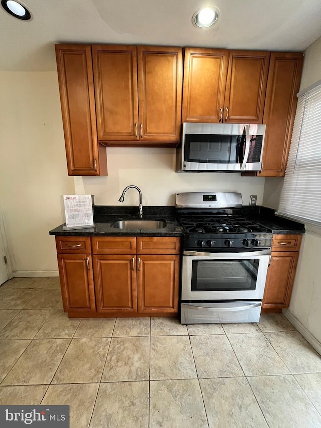 kitchen with light tile patterned floors, stainless steel appliances, dark stone countertops, and sink