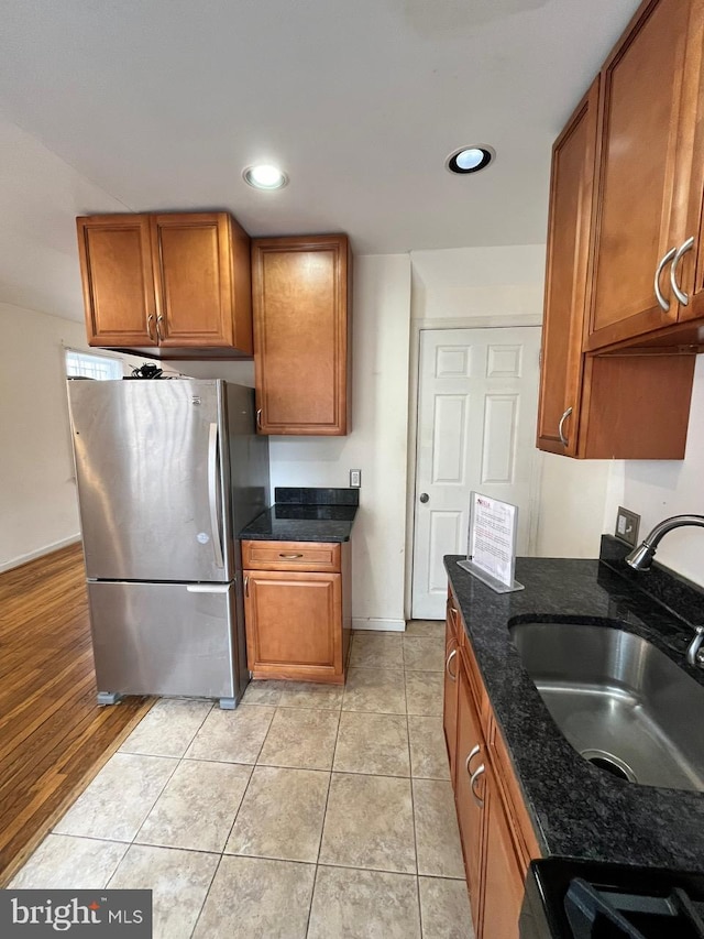 kitchen featuring sink, light hardwood / wood-style flooring, dark stone countertops, stainless steel fridge, and stove