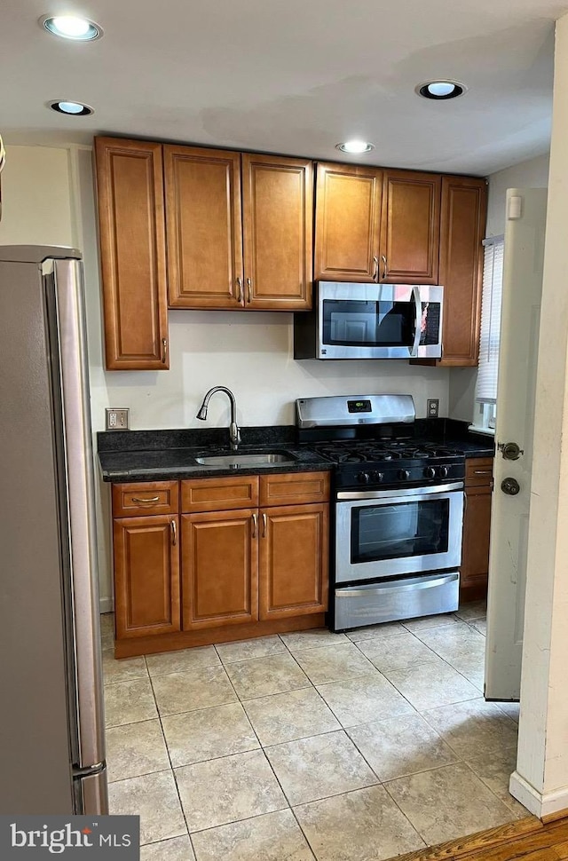 kitchen featuring appliances with stainless steel finishes, light tile patterned floors, dark stone counters, and sink