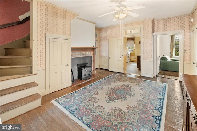 living room featuring ceiling fan, crown molding, a wood stove, and dark wood-type flooring