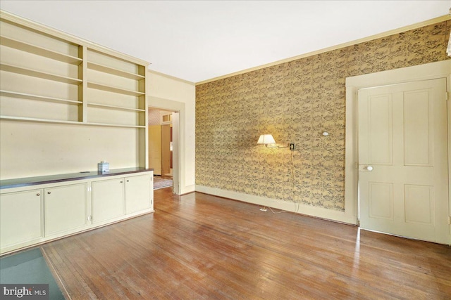 unfurnished living room featuring wood-type flooring and crown molding