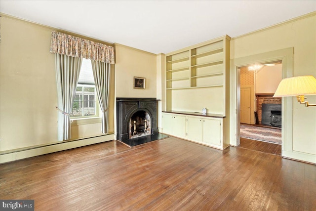 unfurnished living room featuring hardwood / wood-style floors, built in shelves, crown molding, and a baseboard heating unit