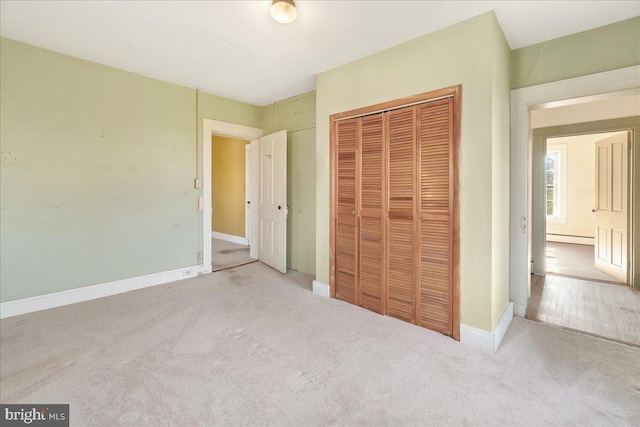 unfurnished bedroom with light colored carpet, a closet, and a baseboard heating unit