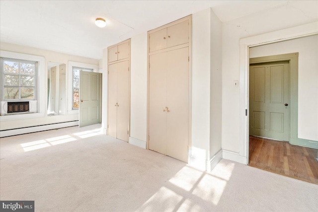 unfurnished bedroom with cooling unit, light colored carpet, and a baseboard heating unit