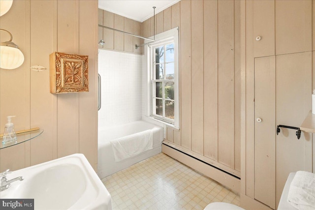 bathroom with tiled shower / bath combo, baseboard heating, wood walls, and sink