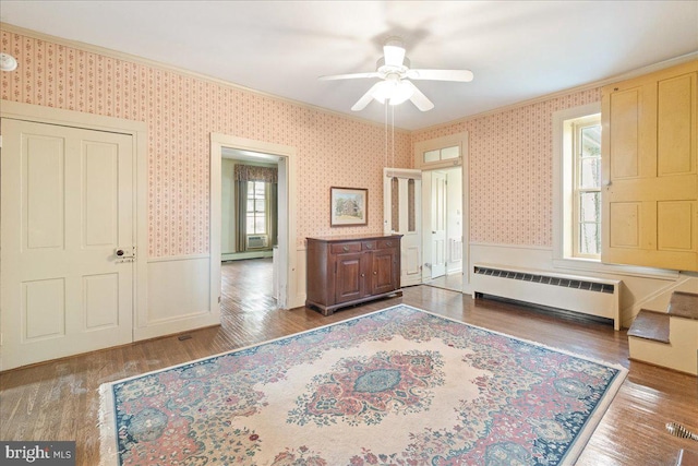 unfurnished bedroom featuring multiple windows, hardwood / wood-style flooring, ceiling fan, and a baseboard heating unit