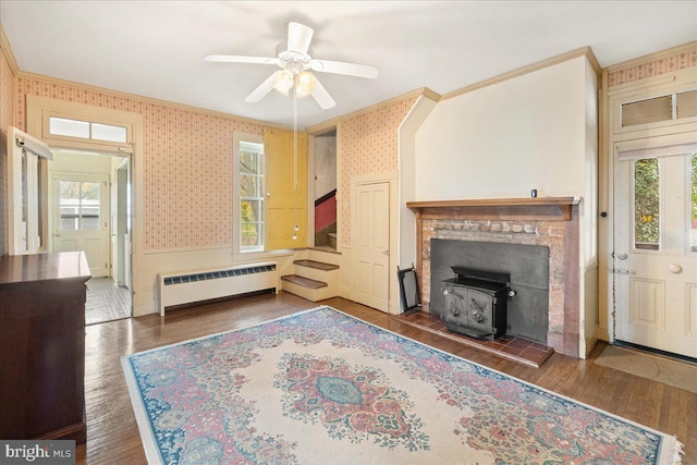 living room with a wood stove, dark wood-type flooring, radiator, ceiling fan, and a healthy amount of sunlight