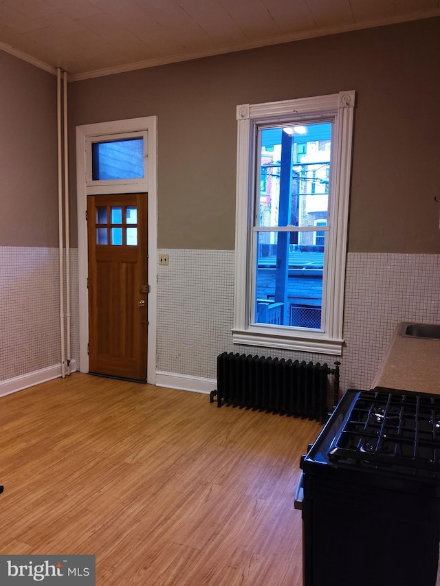 foyer entrance featuring tile walls, radiator heating unit, crown molding, and light hardwood / wood-style flooring