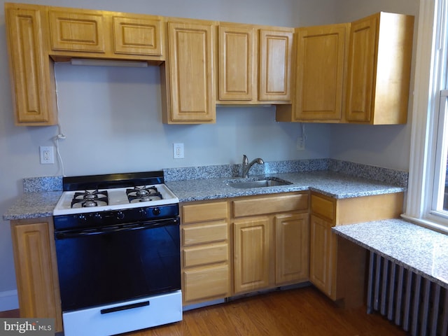 kitchen featuring sink, radiator heating unit, light stone counters, white range oven, and wood-type flooring