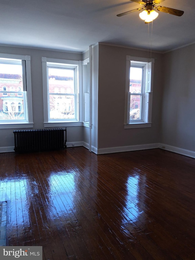 spare room featuring ceiling fan, radiator heating unit, dark wood-type flooring, and a wealth of natural light