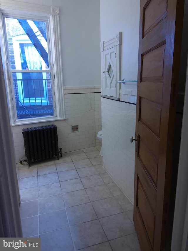 bathroom with tile patterned flooring, radiator heating unit, toilet, and tile walls