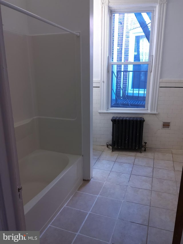 bathroom with tile patterned floors, radiator, a washtub, and tile walls