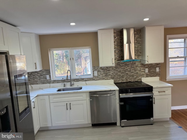 kitchen with white cabinets, plenty of natural light, wall chimney range hood, and appliances with stainless steel finishes