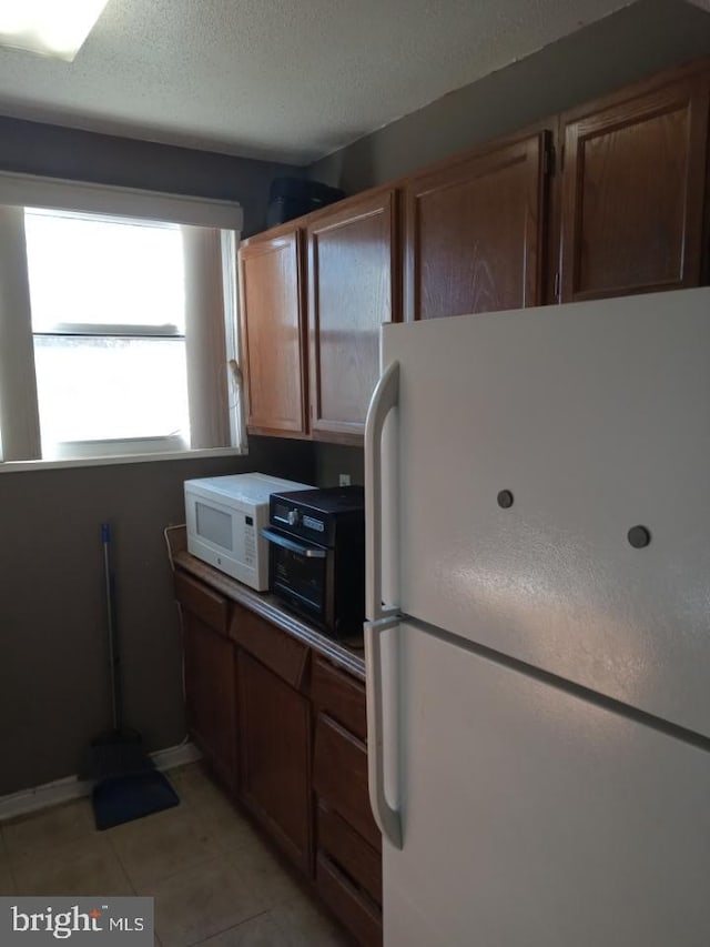 kitchen with white appliances, a textured ceiling, and light tile patterned floors