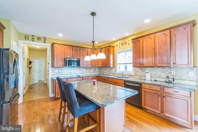 kitchen with sink, a center island, pendant lighting, black appliances, and light wood-type flooring