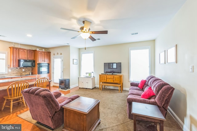 living room featuring ceiling fan, light hardwood / wood-style floors, and a wood stove