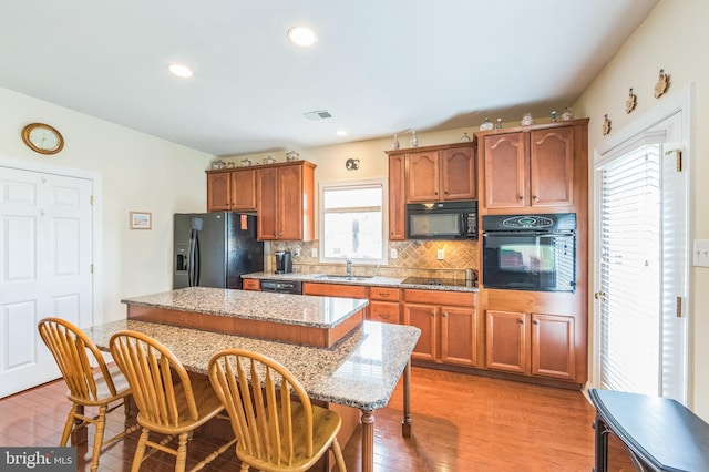 kitchen with a center island, a kitchen bar, black appliances, sink, and light stone counters