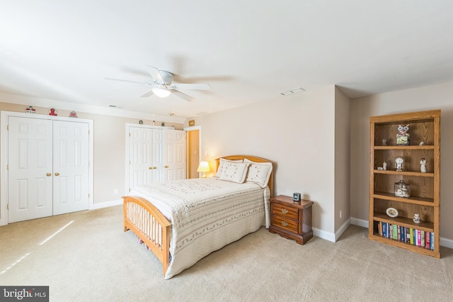 bedroom with light carpet, ceiling fan, and multiple closets