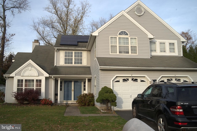 view of front of home with a front yard, solar panels, and a garage