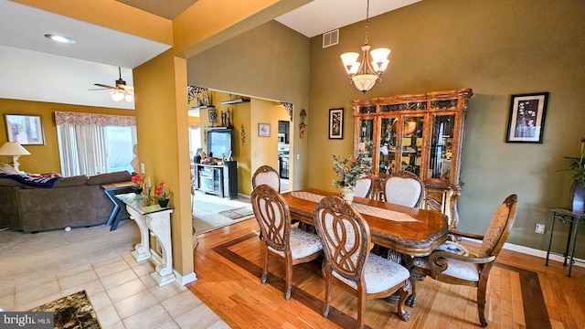 dining space featuring light hardwood / wood-style flooring, a towering ceiling, and ceiling fan with notable chandelier