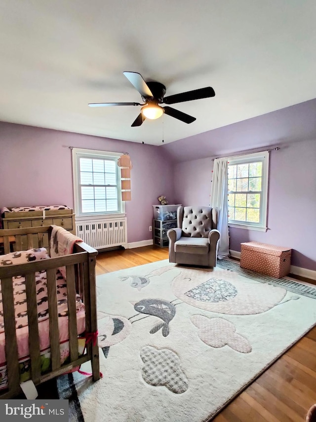 bedroom featuring ceiling fan, radiator heating unit, multiple windows, and light hardwood / wood-style flooring