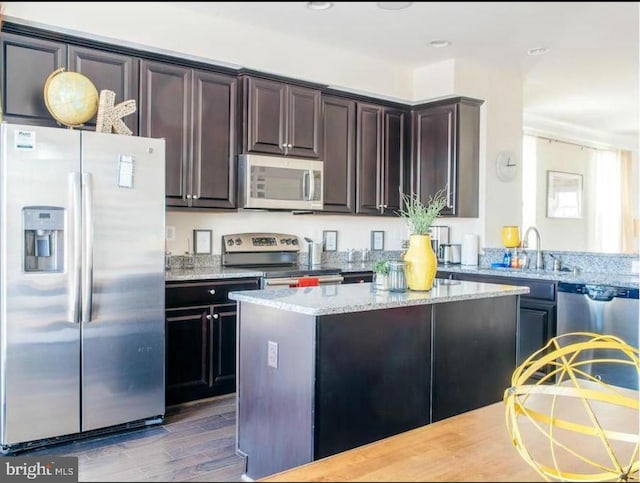 kitchen with light stone countertops, dark brown cabinetry, stainless steel appliances, sink, and hardwood / wood-style flooring