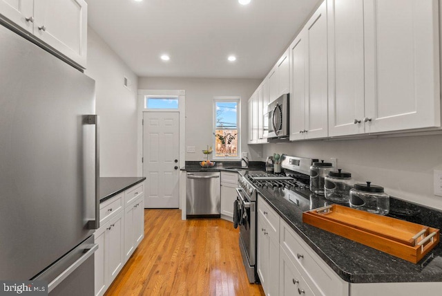 kitchen featuring dark stone counters, white cabinets, sink, light hardwood / wood-style flooring, and stainless steel appliances