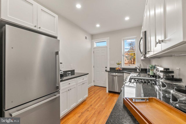 kitchen with white cabinetry, sink, stainless steel appliances, light hardwood / wood-style flooring, and dark stone countertops