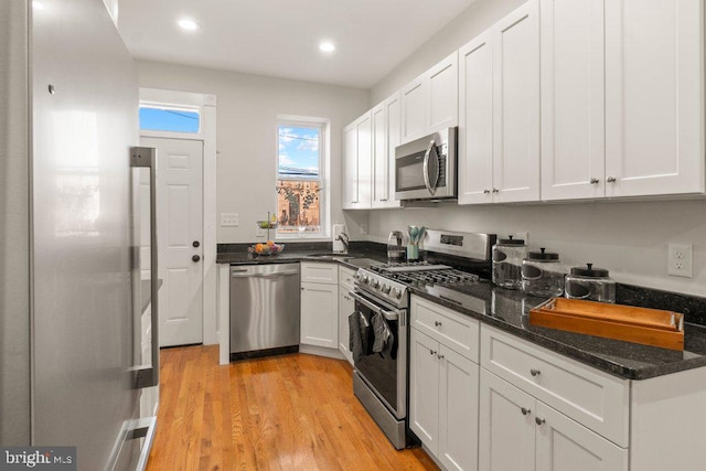 kitchen featuring dark stone countertops, white cabinetry, light wood-type flooring, and appliances with stainless steel finishes