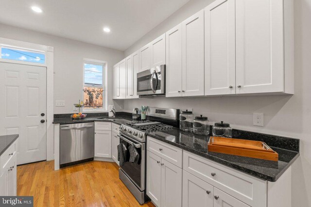 kitchen featuring dark stone countertops, white cabinets, stainless steel appliances, and light hardwood / wood-style floors