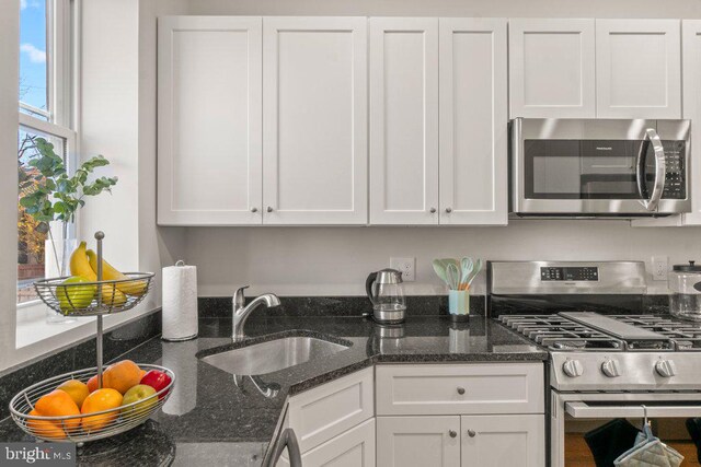 kitchen with sink, white cabinetry, stainless steel appliances, and dark stone counters