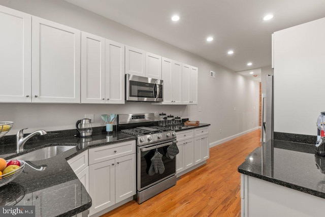 kitchen featuring white cabinets, stainless steel appliances, dark stone countertops, and sink