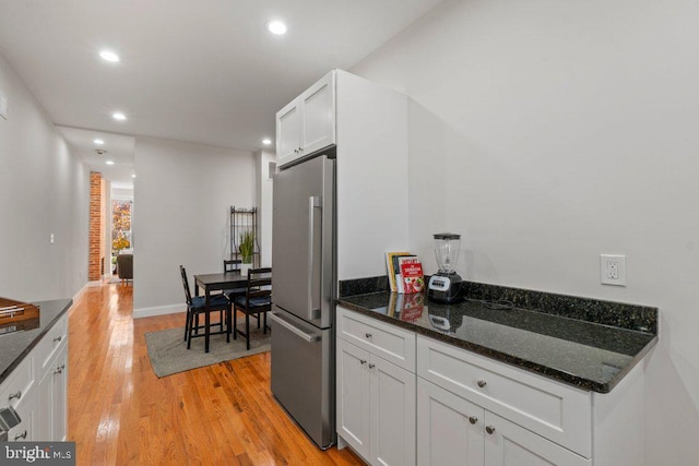 kitchen with white cabinets, stainless steel fridge, light hardwood / wood-style flooring, and dark stone countertops