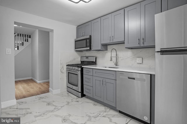 kitchen with sink, light hardwood / wood-style flooring, gray cabinets, decorative backsplash, and appliances with stainless steel finishes