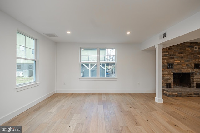 unfurnished living room with plenty of natural light, a stone fireplace, and light hardwood / wood-style flooring