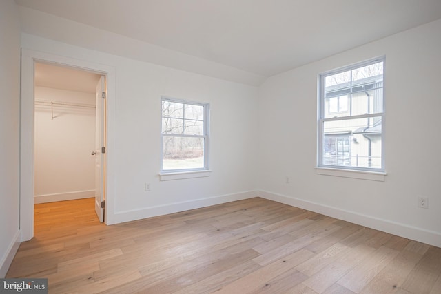 unfurnished bedroom featuring multiple windows, a spacious closet, a closet, and light wood-type flooring