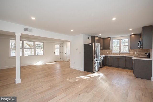 kitchen with sink, decorative backsplash, light wood-type flooring, dark brown cabinetry, and stainless steel appliances