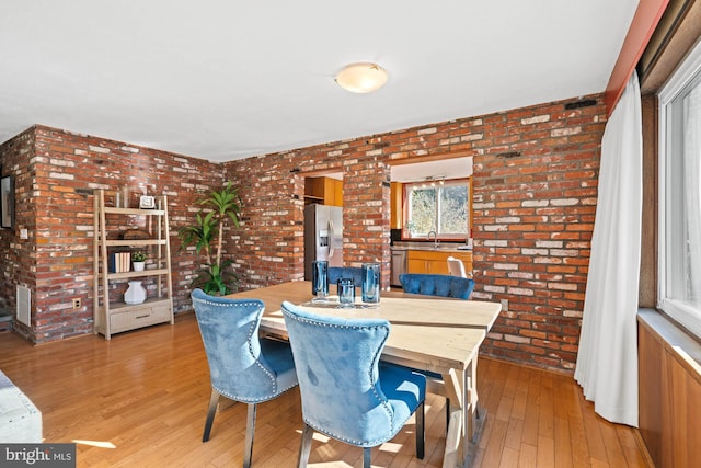 dining space featuring sink, light hardwood / wood-style floors, and brick wall