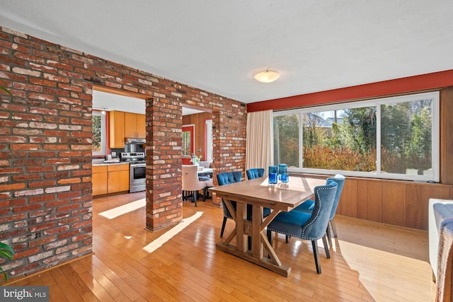 dining area with light hardwood / wood-style flooring, decorative columns, and brick wall