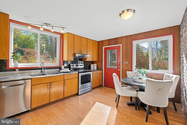 kitchen with sink, appliances with stainless steel finishes, wooden walls, tasteful backsplash, and light wood-type flooring