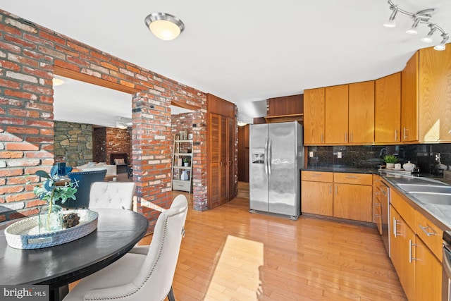 kitchen with brick wall, tasteful backsplash, sink, stainless steel fridge, and light hardwood / wood-style flooring